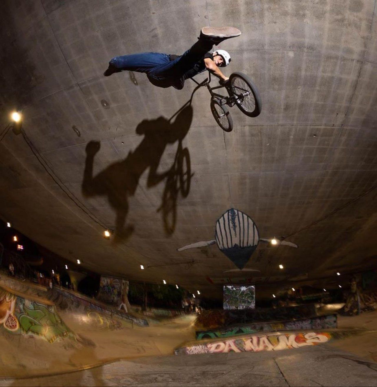 Robin Meza springt nachts in einer überdachten Betonbowl hoch in die Luft, sein Schatten fällt groß auf die gewölbte Wand.