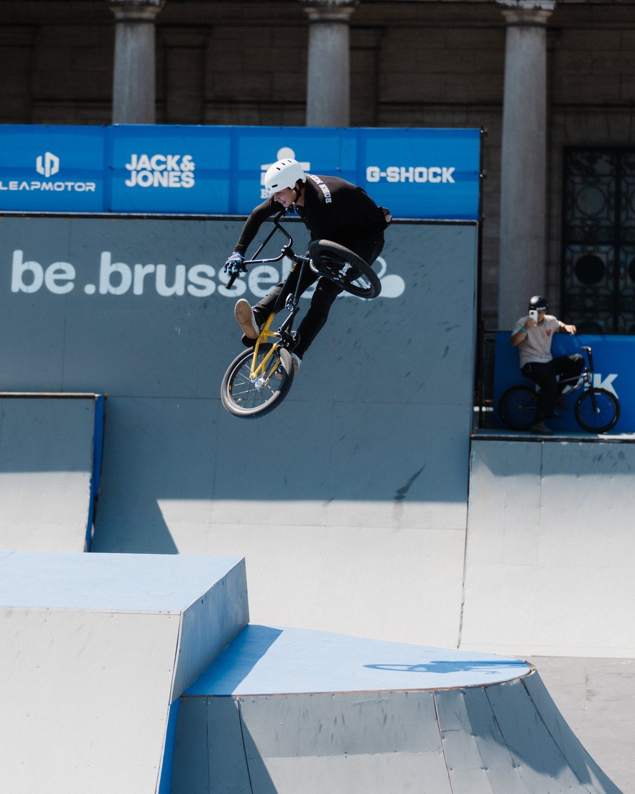 Robin Meza mit weißem Helm bei einem Trick über einer Contest-Rampe, im Hintergrund Sponsorenbanner mit der Aufschrift be.brussels.