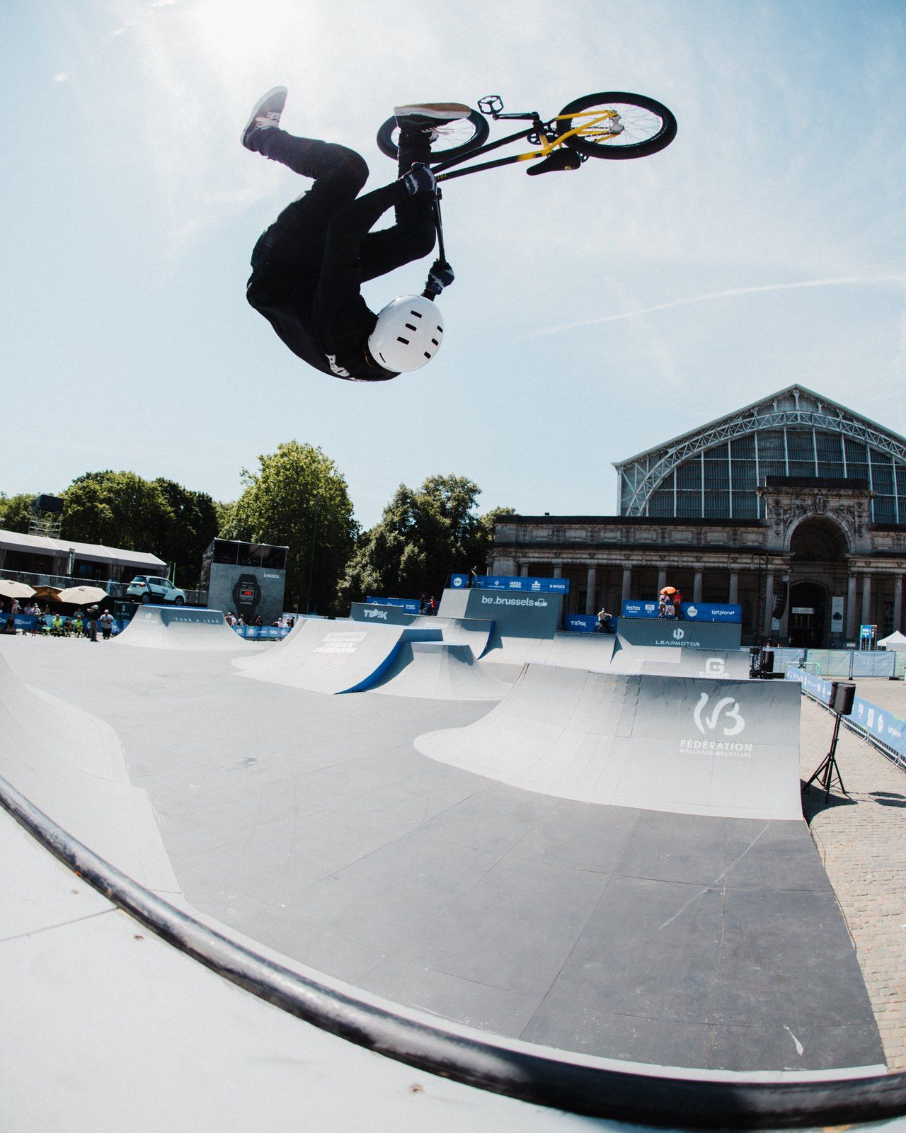 Robin Meza kopfüber mit seinem BMX-Rad hoch über einem Contest-Parcours, im Hintergrund Zuschauer und eine historische Halle.