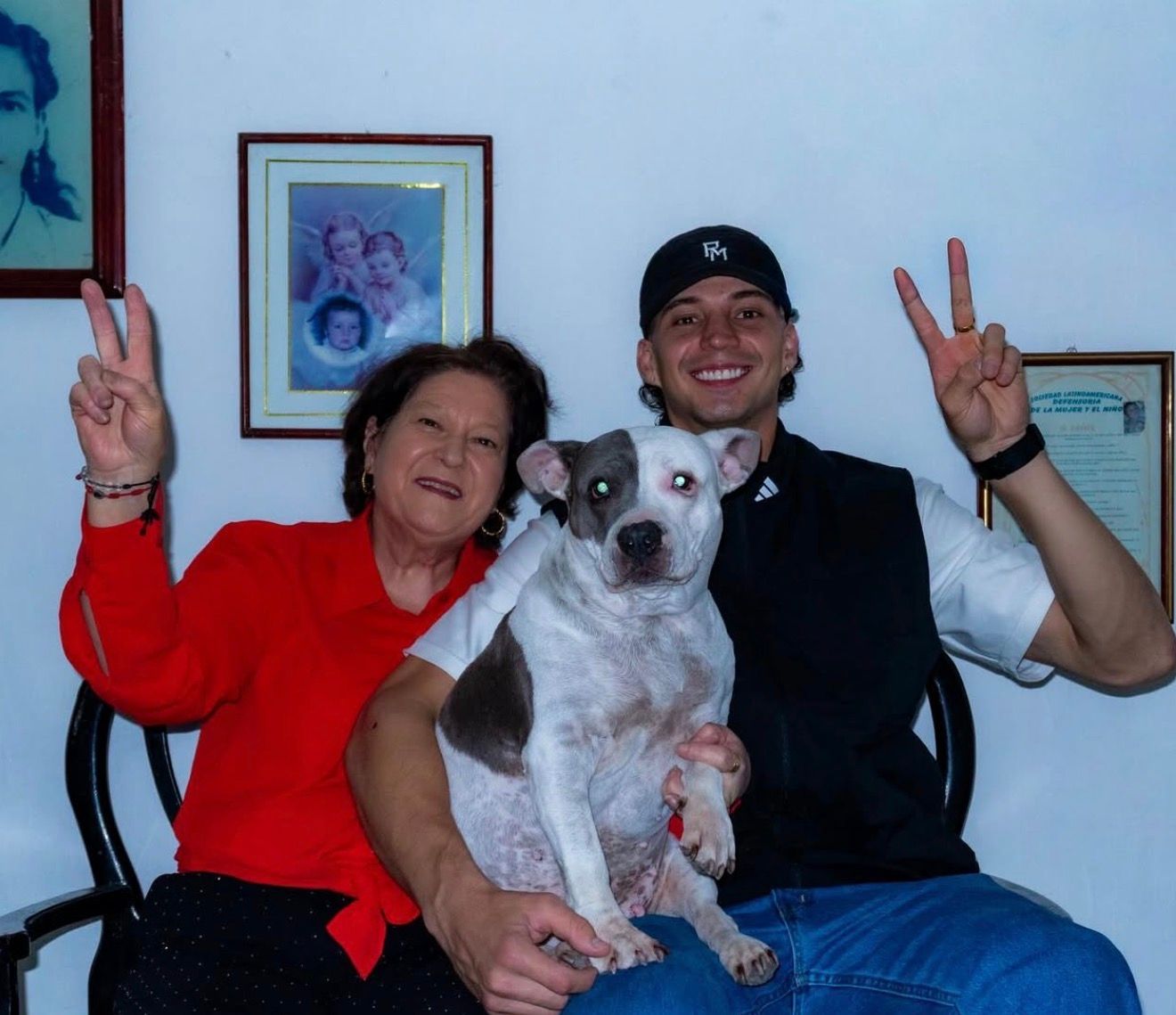 Robin und seine Mutter sitzen zu Hause nebeneinander, zwischen ihnen ein grau-weißer Hund. Beide lachen und zeigen das Peace-Zeichen.