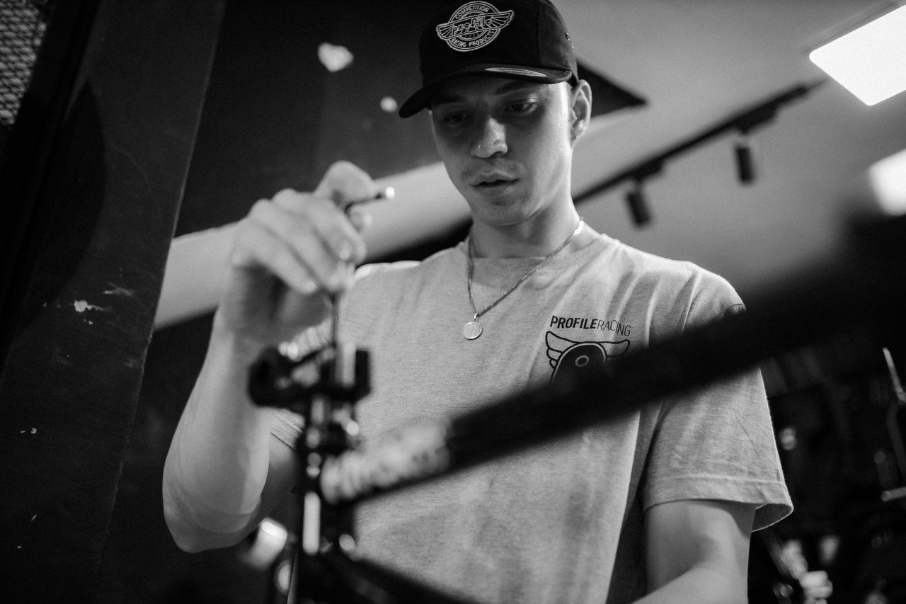 Schwarz-Weiß-Aufnahme: Robin Meza mit Cap und T-Shirt schraubt konzentriert am Lenker seines BMX-Rads.